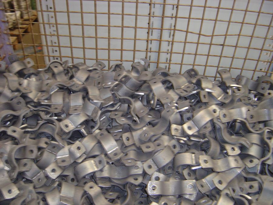 Verzinkte Schellenhälften nach DIN 3567 als Massenware in einer Gitterbox im Lager